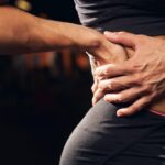 Persona con ropa deportiva llevándose la mano a la zona lumbar por dolor de espalda baja