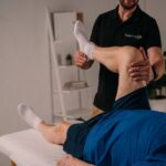 Fisioterapeuta de FisiomadFit movilizando la rodilla de un paciente tumbado en la camilla durante una sesión a domicilio en Madrid