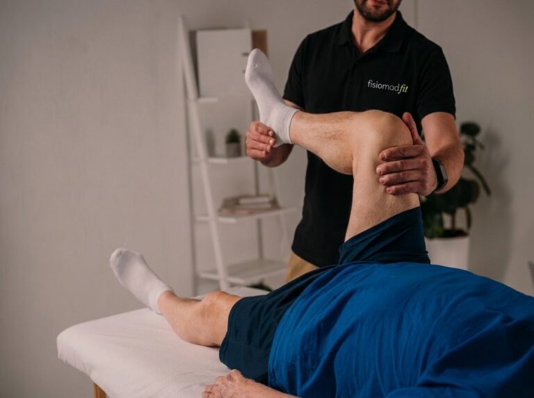Fisioterapeuta de FisiomadFit movilizando la rodilla de un paciente tumbado en la camilla durante una sesión a domicilio en Madrid