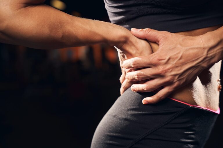 Persona con ropa deportiva llevándose la mano a la zona lumbar por dolor de espalda baja