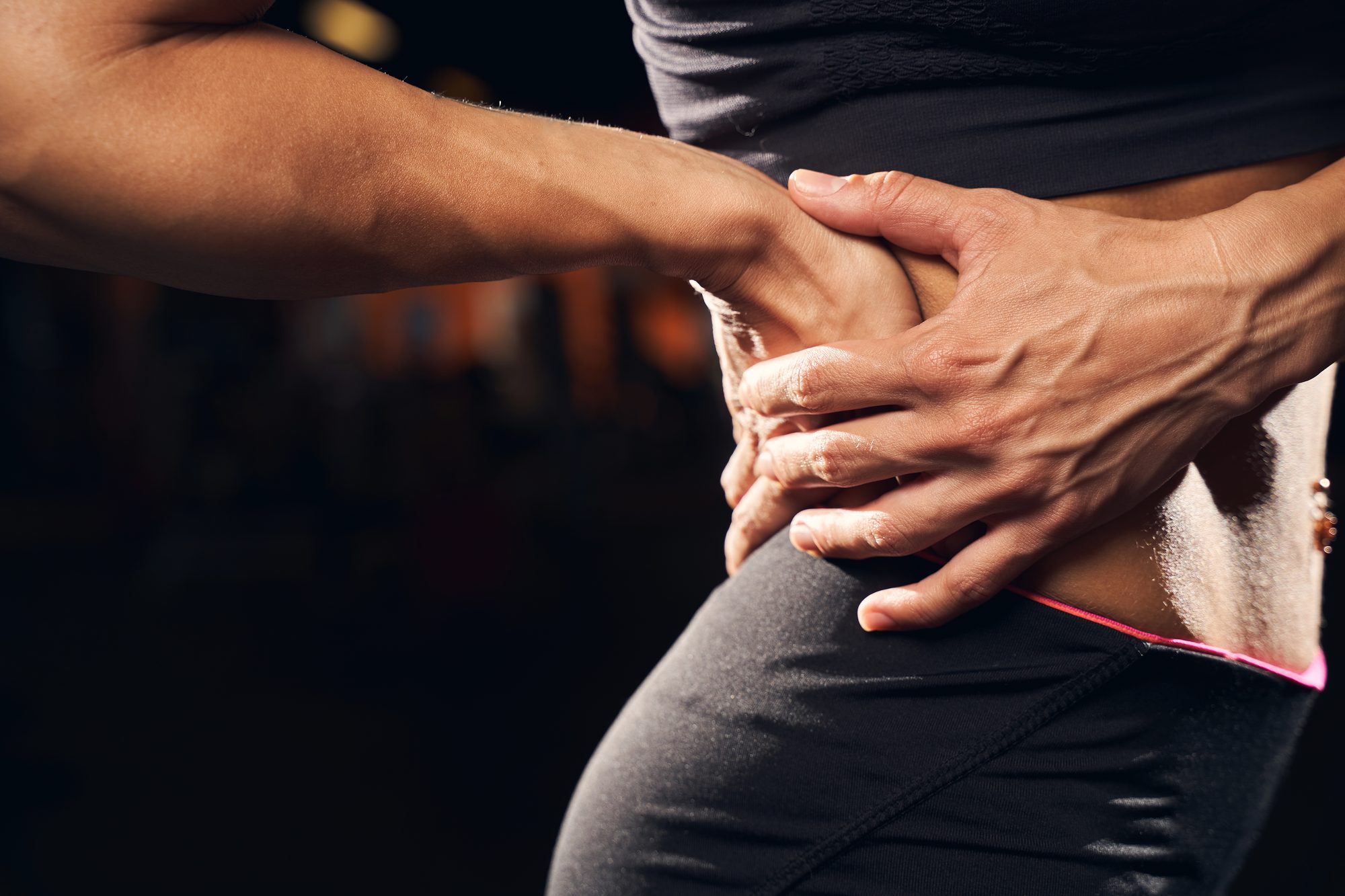 Persona con ropa deportiva llevándose la mano a la zona lumbar por dolor de espalda baja